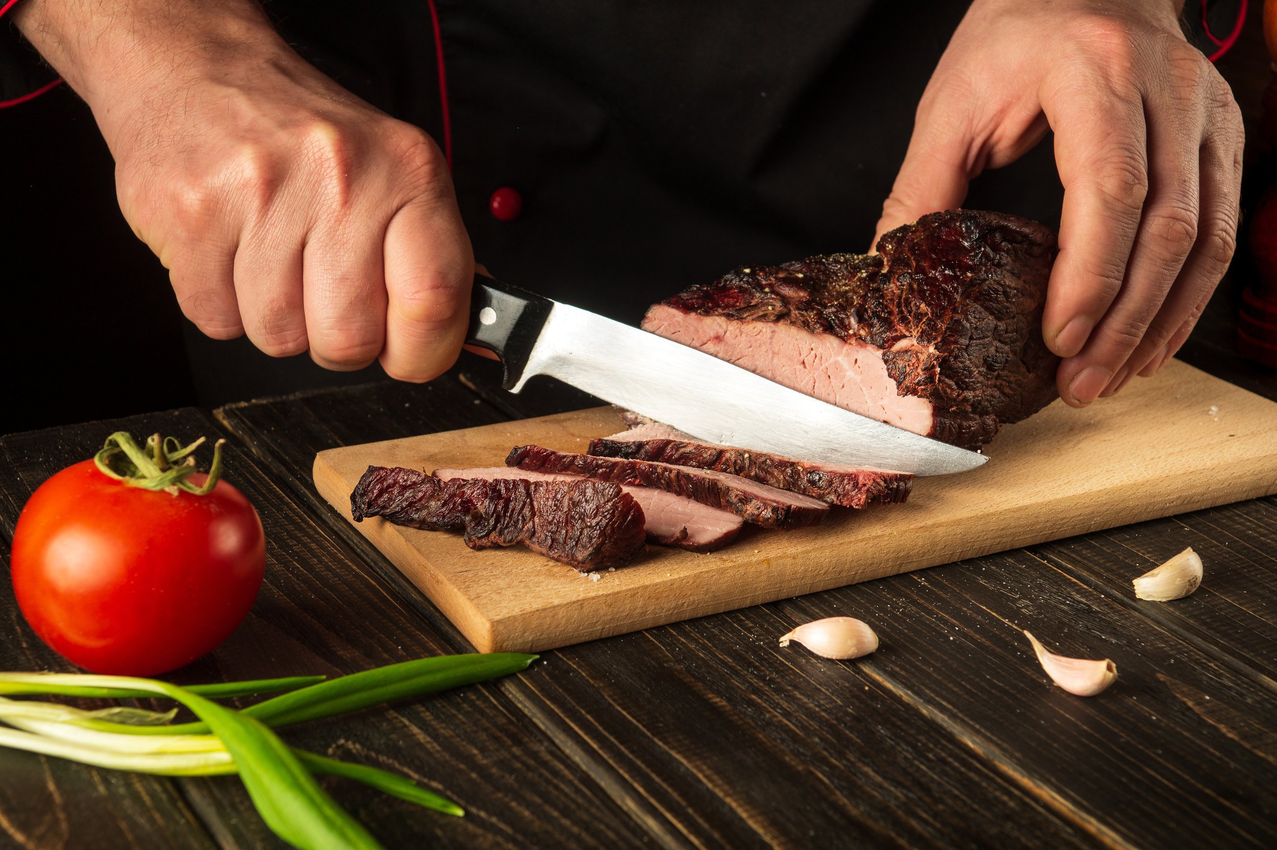 The cook cuts the baked veal meat on a cutting board. The concep